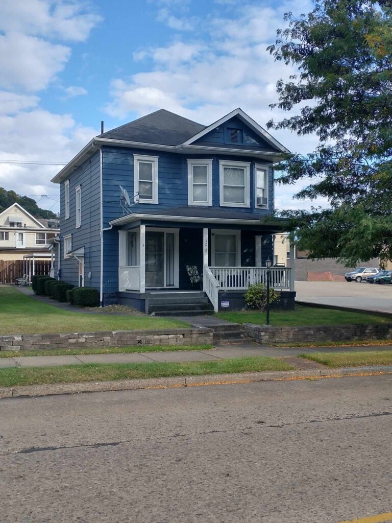 A charming blue house with a porch and a white picket fence, creating a picturesque and inviting scene.