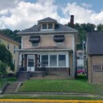 A charming two-story brick house with a porch and a front yard, exuding a sense of warmth and homeliness.