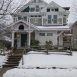 Spacious house with white roof and green porch, surrounded by snow-covered yard.